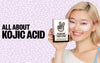 "All About Kojic Acid" over a pink background with a young woman wearing Peace Out Puffy Eyes and holding the box.