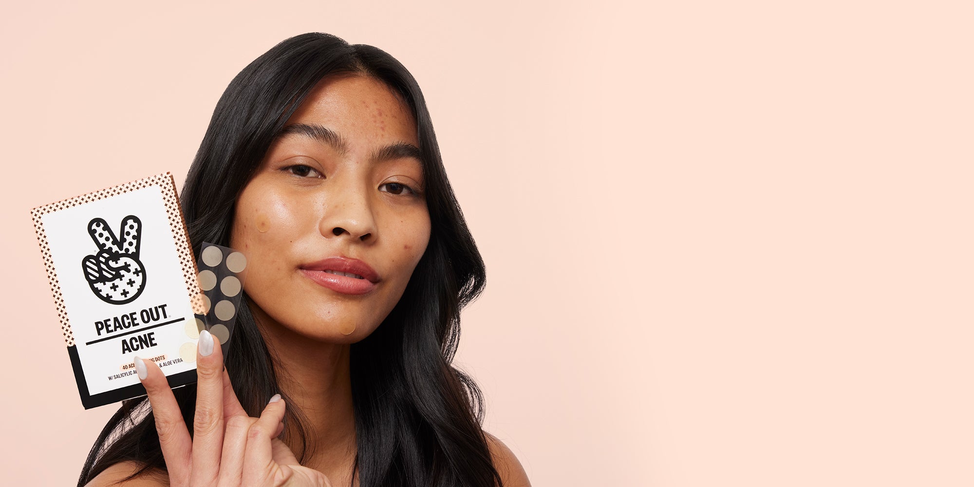 A woman holds up Peace Out Acne Healing Dots against a peach background

